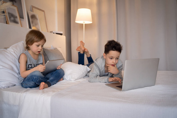 Deux enfants, garçons dans le lit des parents le matin avec ordinateur portable et tablette. Les frères jouent à des jeux informatiques. Frères et soeurs et gadgets
. - Photo, image