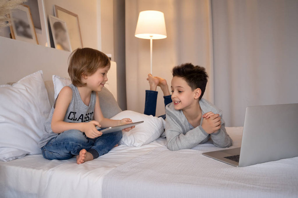 Two children, boys in parents bed at morning with laptop and tablet. Brothers play computer games. Siblings and gadgets. - 写真・画像