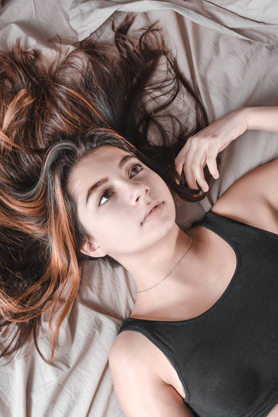 κορίτσι με μακρύ ρέει μαλλιά ξαπλωμένος στο κρεβάτι και εξετάζοντας σκεπτικώς - Φωτογραφία, εικόνα