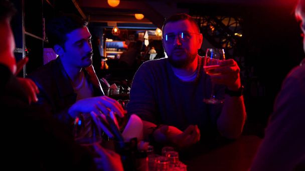 Бар з неоновим освітленням. Група друзів, які сидять за столом і п'ють алкоголь під час розмови
 - Фото, зображення