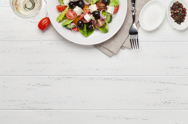 Греческий салат с огурцами, помидорами, перцем, салатом, луком, сыром фета и оливками в белой тарелке на деревянном фоне
  - Фото, изображение