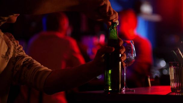 Bar con iluminación de neón. Un hombre abre una botella de cerveza
 - Foto, Imagen