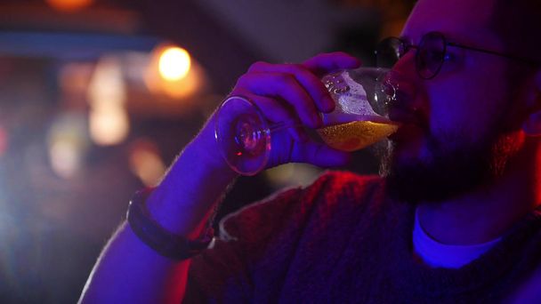 Бар с неоновым освещением. Человек, пьющий стакан пива
 - Фото, изображение
