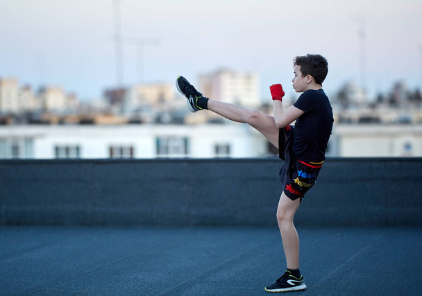 Boy fighter training on roof with buildings in blurred background - Foto, afbeelding