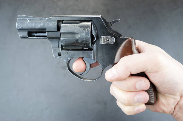Hand holding a revolver, finger on the trigger. Blurred background - Photo, Image
