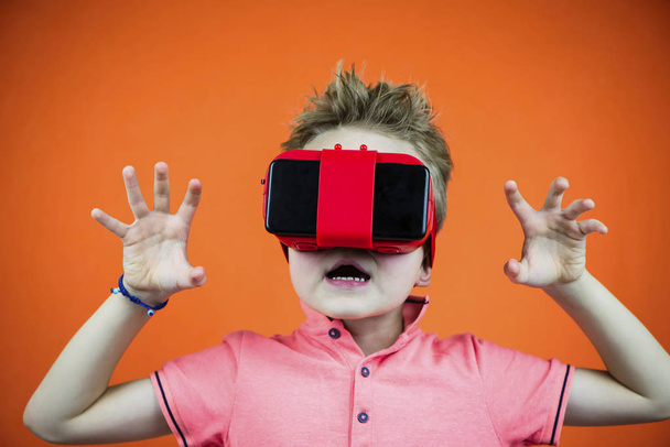 funny boy in virtual reality glasses playing smartphone on orange background - Foto, imagen
