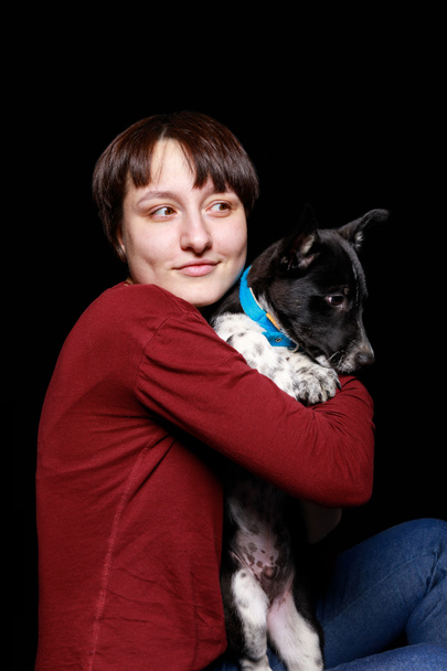 γυναίκα στο κόκκινο πουλόβερ αγκάλιασμα και κρατώντας μιγάς σκυλί στο μπλε κολάρο που απομονώνονται σε μαύρο - Φωτογραφία, εικόνα