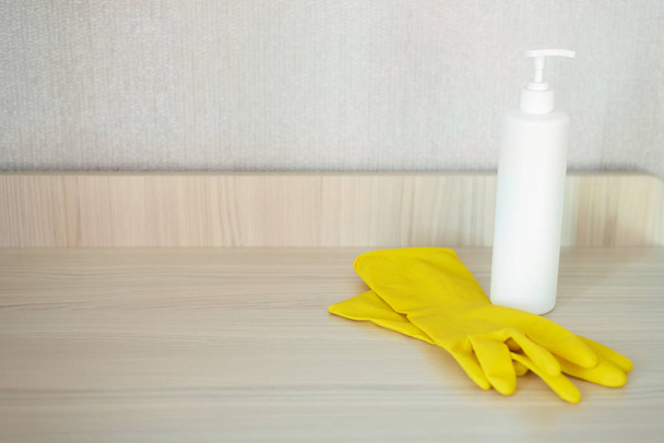 White dishwashing soap and a yellow protective gloves on a kitchen table background with copy space. - Foto, imagen