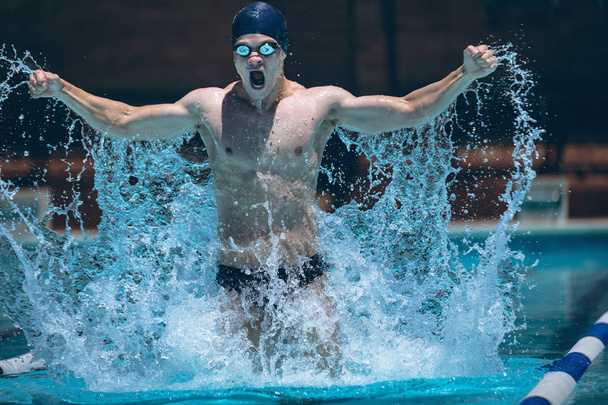 Front view of young Caucasian male swimmer with arms stretched out celebrate victory in pool in the sunshine - Photo, Image