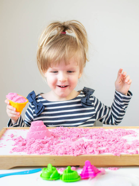 Маленькая счастливая белая девочка, играющая с розовым кинетическим песком дома
 - Фото, изображение