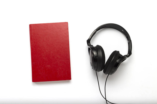 Buch mit rotem Einband und schwarzen Kopfhörern auf weißem Hintergrund - Foto, Bild