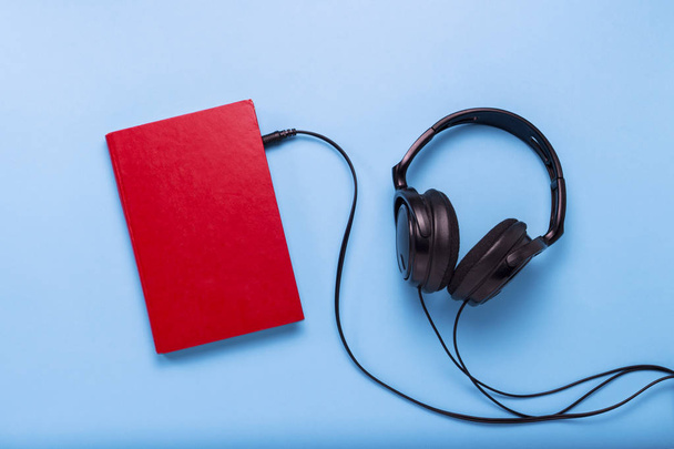 Buch mit rotem Einband und schwarzen Kopfhörern auf blauem Hintergrund. - Foto, Bild