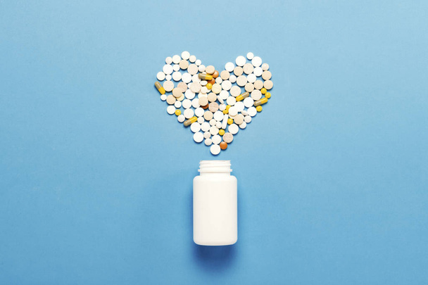 White bottle and multi-colored pills in shape of a heart. Blue b - Φωτογραφία, εικόνα