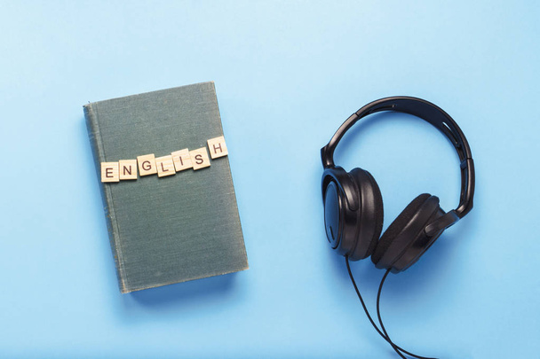 Buch mit blauem Einband mit englischem Text und schwarzen Kopfhörern - Foto, Bild
