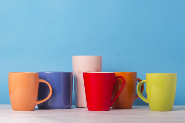Многие разноцветные чашки кофе или чая на синем фоне. Концепция дружелюбной компании, большой семьи, встречи с друзьями за чашкой чая или кофе
 - Фото, изображение