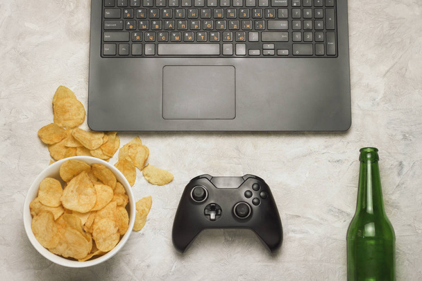 Laptop, Gamepad, aardappels, chips, fles of Beer op een lichte stenen b - Foto, afbeelding