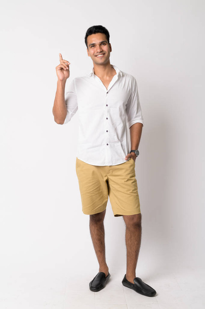 Full body shot of happy young handsome Indian man pointing up - Foto, afbeelding