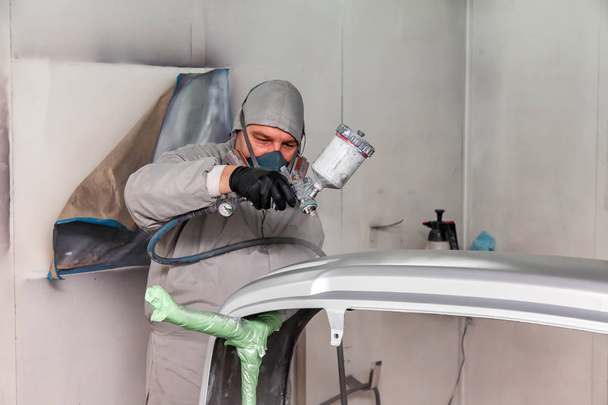 Een mannelijke werknemer schildert met een spuitpistool een deel van het autolichaam in  - Foto, afbeelding
