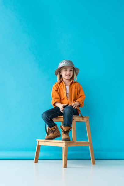smiling kid in jeans and orange shirt sitting on stairs and looking at camera  - Fotoğraf, Görsel
