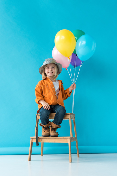 cute kid in jeans and orange shirt sitting on stairs and holding ballons  - Foto, Imagem