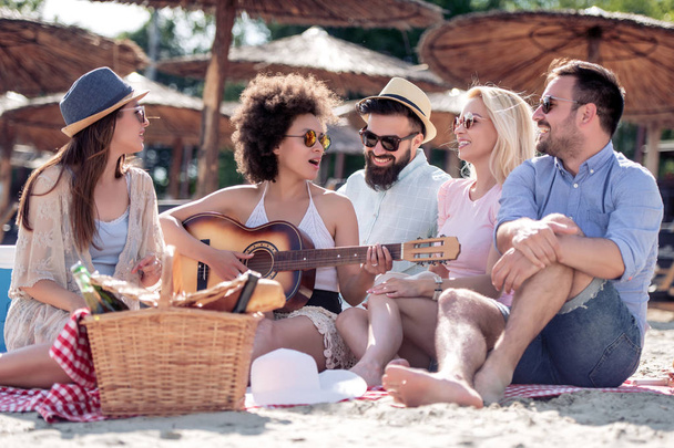 Gruppe fröhlicher junger Leute, die am Strand picknicken und zusammen Spaß haben. - Foto, Bild