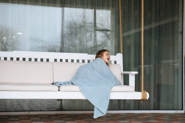 Маленька блондинка, загорнута в ковдру і лежить на дивані
 - Фото, зображення