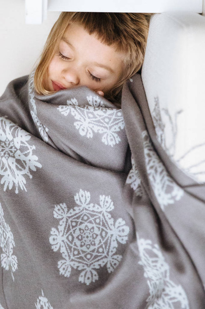 Little blonde girl wrapped in blanket and lying on sofa - Valokuva, kuva