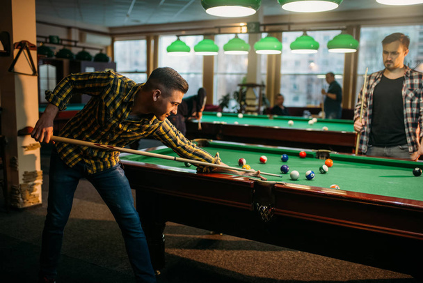 Two male billiard players with cue at the table with colorful balls. Men plays american pool in sport bar - Foto, afbeelding