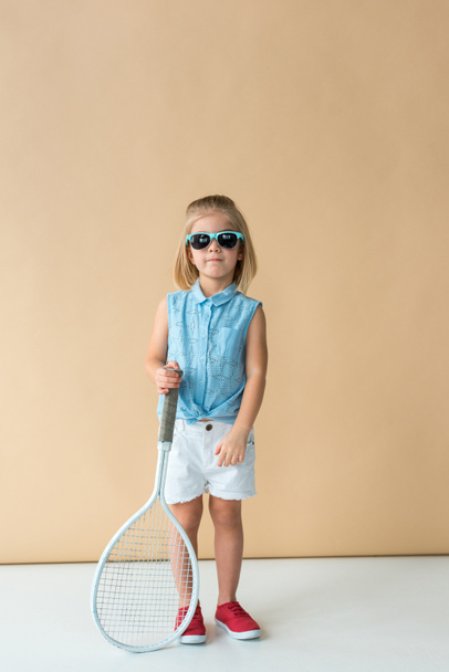 cute kid in sunglasses, shirt and shorts holding racket and looking at camera  - Fotoğraf, Görsel