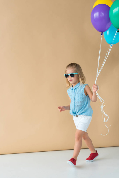 carino bambino in occhiali da sole, camicia e pantaloncini a piedi e tenendo palloncini
 - Foto, immagini