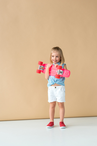 niño sonriente y lindo en camisa y pantalones cortos con tablero de penique rosa sobre fondo beige
  - Foto, imagen