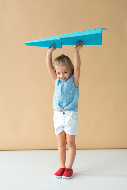 adorabile e sorridente bambino in camicia e pantaloncini con in mano aereo di carta blu
  - Foto, immagini
