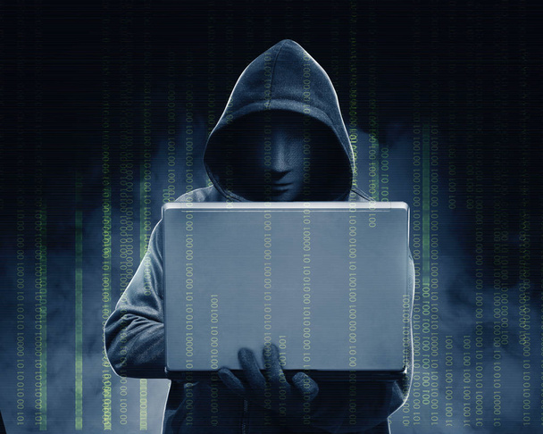 Hacker in black hoodie holding laptop with his hand and binary c - Foto, afbeelding