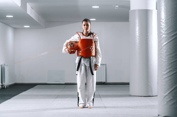 Beautiful Caucasian young woman with ponytail standing in taekwondo fitting and looking at camera. - Photo, Image