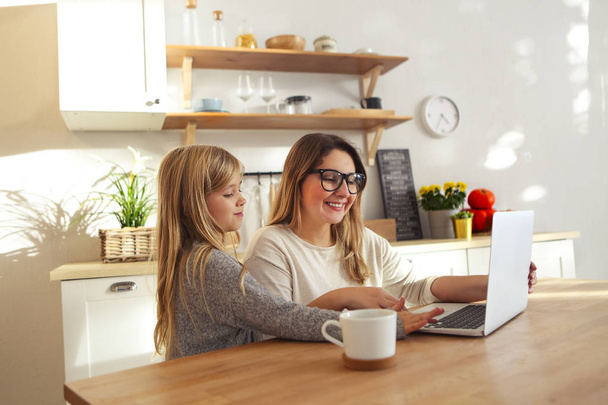 mãe com menina usando laptop na cozinha
  - Foto, Imagem