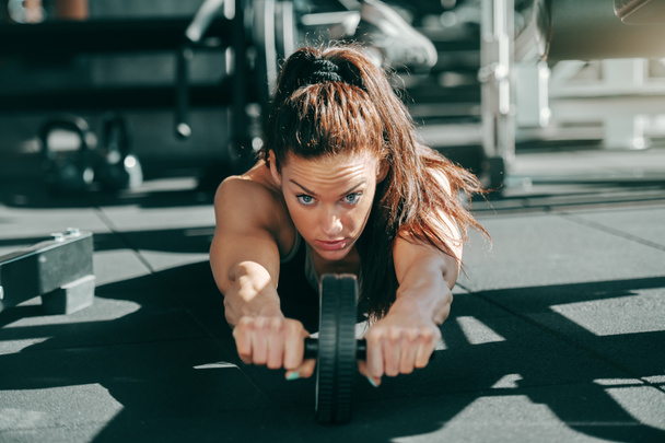 Young attractive sporty female bodybuilder with ponytail doing exercises for abs on gym floor. Don't give up just because of what someone said, use that as motivation to push harder. - Photo, Image