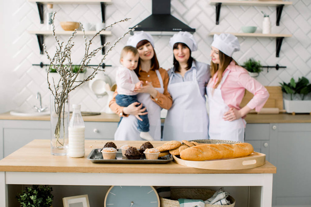three generations of women are cooking in the kitchen, focus on the table with maffines and cookies. Homemade food and little helper. Happy family. Baking in kitchen. Easter holidays or mothers day - 写真・画像
