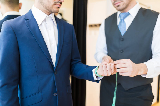 Midsection of creative young seamster measuring wrist of wealthy man in clothing store - Photo, Image