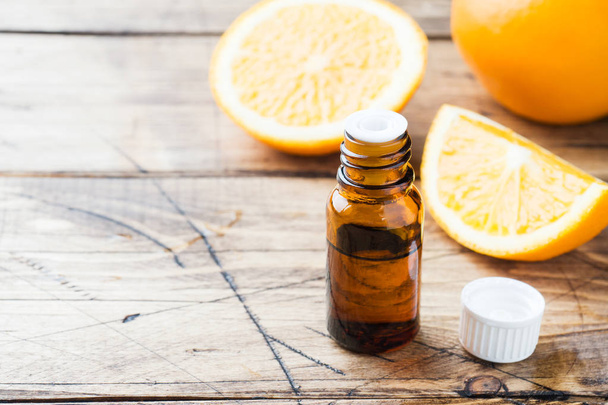 Essential orange oil in bottle, fresh fruit slices on wooden background. Natural fragrances. - 写真・画像