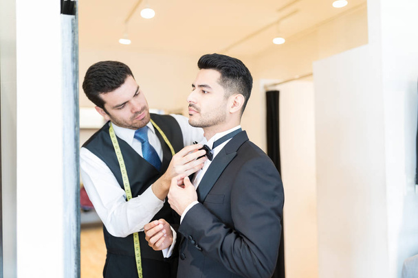 Клерк настраивает галстук-бабочку на клиента, стоя в магазине проката костюмов
 - Фото, изображение