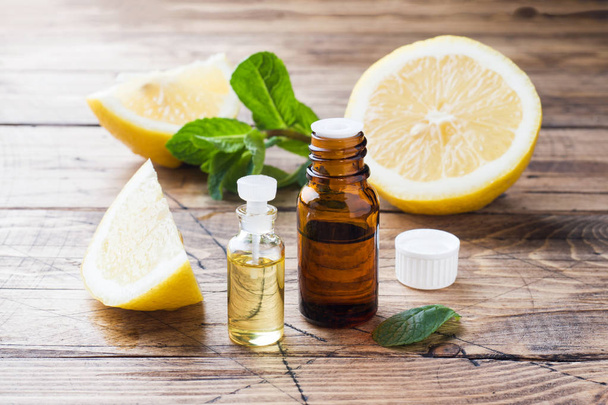 Essential lemon oil in bottle, fresh fruit slices on wooden background. Natural fragrances. - Фото, изображение