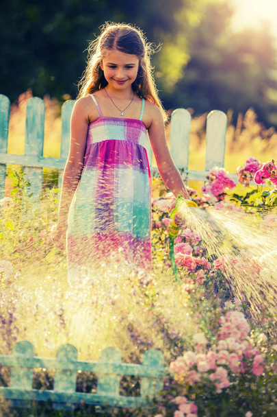 Dziewczyna playfull podlewanie kwiatów deszcz w ogrodzie w letni - Zdjęcie, obraz