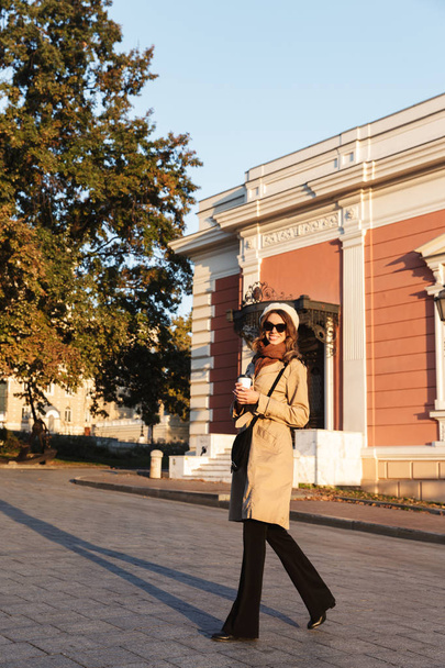 Happy young beautiful woman walking outdoors drinking coffee at the street. - Valokuva, kuva