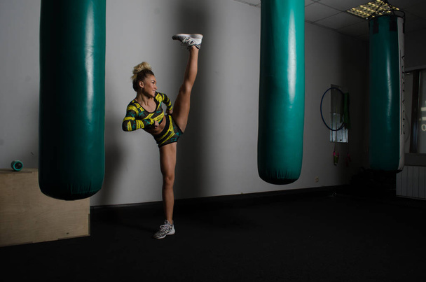 kickboxer en ropa deportiva y vendajes está lanzando golpes con piernas y brazos en el entrenamiento
 - Foto, Imagen