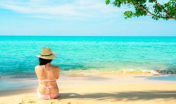 ピンクの水着と麦わら帽子のリラックスで幸せな若いアジア女性の背面し、バカンス熱帯の楽園ビーチで休日をお楽しみください。休暇の夏のファッションの女の子。美しさセクシーなモデル。夏の感じ. - 写真・画像