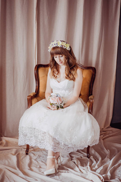 Portrait of happy young bride sitting on a armchair in a classic interior. Wedding day, love theme. First day of a new family - Fotó, kép