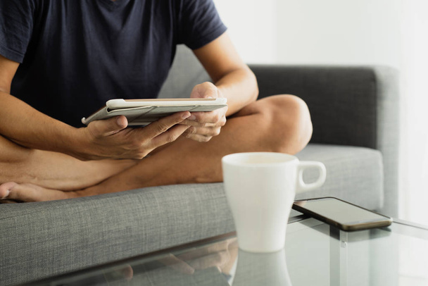 uomo seduto a gambe incrociate su un divano utilizzando un tablet
 - Foto, immagini
