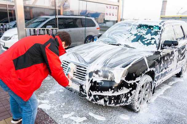 Kırmızı ceketli adamı bir fırça ile köpük kaplı Siyah araba kendi kendine araba yıkamacıda siliyor. Önden Görünüm - Fotoğraf, Görsel