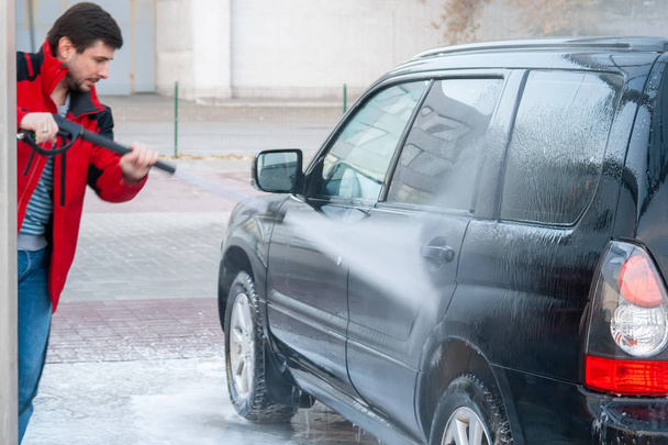 Ένας άνθρωπος πλένει ένα μαύρο αυτοκίνητο με μια ισχυρή εκτόξευση του νερού σε ένα πλυντήριο αυτοκινήτων σελφ-σέρβις - Φωτογραφία, εικόνα