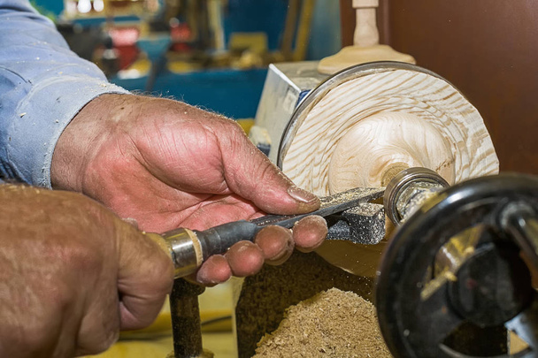 Работать плотником на токарном станке на дереве. Крупный план мужских рук зубилом при обработке деревянного бланка
. - Фото, изображение
